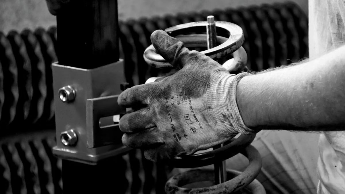 Close-up of a gloved auto mechanic's hand working with a spring in a workshop.